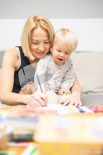 Image of Caring young Caucasian mother and small son drawing painting in notebook at home together. Loving mom or nanny having fun learning and playing with her little 1,5 year old infant baby boy child.