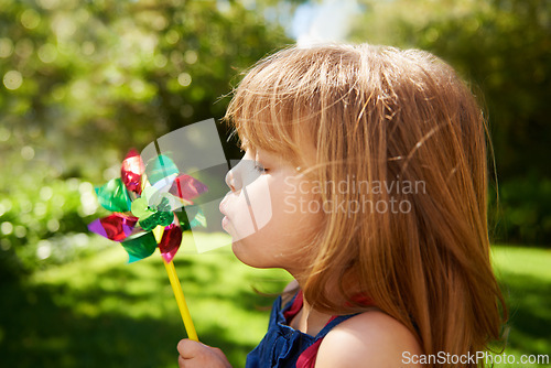 Image of Young girl, outdoor and blowing pinwheel, garden and enjoying freedom of outside and happy. Pretty little child, backyard and summer for playing, toy and windmill for school holidays and happiness