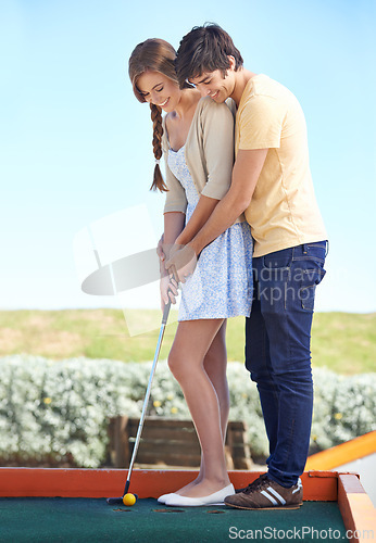 Image of Young couple, love and outdoor for mini golf in nature, bonding together and happy on weekend with hobby. Man, woman and putt on romantic trip and care, sunshine and teaching girlfriend to play game