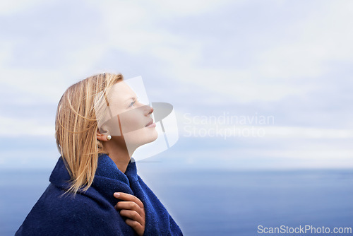 Image of Thinking, ocean and woman with blanket with blue sky for adventure on holiday, vacation and weekend outdoors. Nature, travel and person by seaside for relaxing, happiness and peace in countryside
