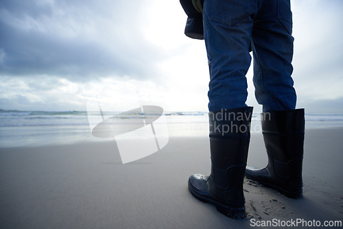 Image of Travel, boots and shoes of person at beach for ocean, tourism and walking in sand. Adventure, vacation and calm with feet of traveler and gumboots at seaside for relax, holiday trip and journey