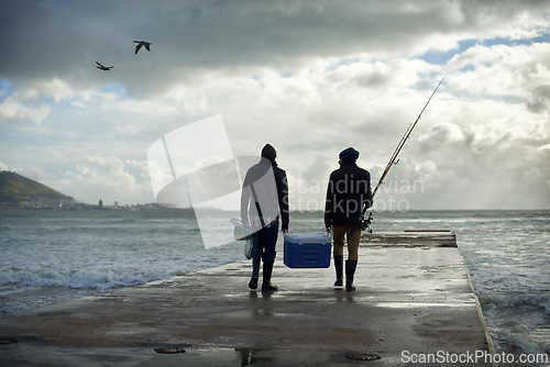 Image of Back, walking and beach with fishermen, cooler box or activity with equipment or weekend break. People, ocean or friends with gear for hobby or rod with waves, talk or seaside with nature and cloudy