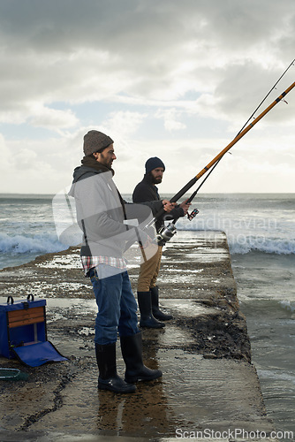 Image of People, fishing and friends at beach on weekend, relaxing and casting a line by ocean. Men, fisherman and cloudy sky on vacation or holiday, hobby and bonding by wave and support on outdoor adventure