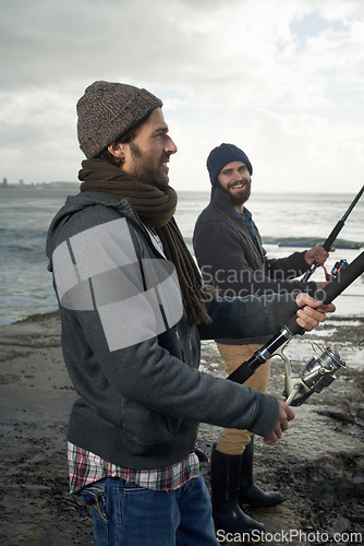 Image of People, sea and friends with fishing pole at beach, relaxing and casting a line by ocean. Men, fisherman and cloudy sky on vacation or holiday, hobby and bonding by waves and support on adventure