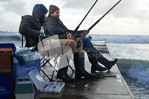 Image of Ocean, pole for fishing and men outdoor in winter, leisure activity at beach or harbor with friends in nature for seafood. Travel, seascape and waves with fisherman, recreation or hobby in the cold