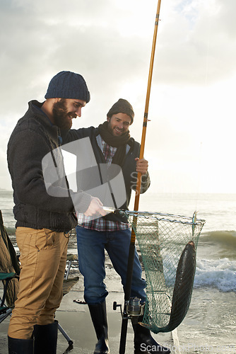 Image of Fishing, friends and net with fish at pier with rod, waves and relax on vacation, holiday and adventure. Friendship, men and bonding in morning with overcast, sky and nature for activity and hobby