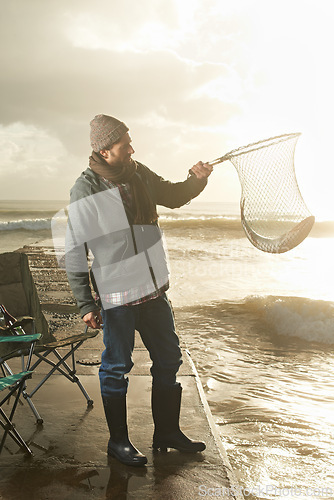 Image of Sunshine, net and beach with man, fish and hobby with equipment, waves and weekend break. Person, ocean and guy with tools for activity and happiness with shore, pier and seaside with lens flare