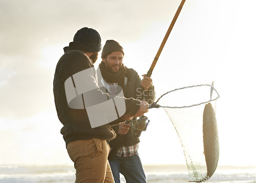 Image of Fishing, men and net with fish at beach with rod, water and relax on vacation, holiday and travel. Friendship, people and bonding in morning with overcast, sky and nature for activity and hobby