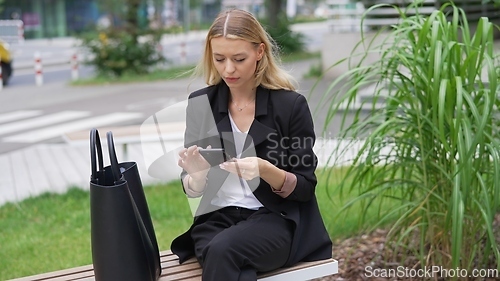 Image of Professional Woman Checking Phone on City Bench