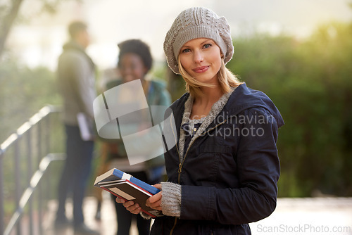 Image of Closeup, winter and university student with book in outdoor on campus, happy and smile with support and care. Education, college with notes to prepare for exam, assessment and texbook to study.