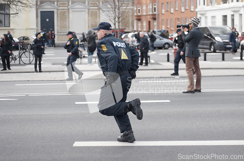 Image of Police officer, man and running in street with crowd safety with protection service for public in city. People, law enforcement and justice in danger, arrest or warning on urban road in Copenhagen