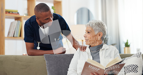 Image of Senior, woman and nurse on sofa with support, conversation and caregiver in living room of retirement home. Elderly, person and black man with kindness, happiness and discussion while reading a book