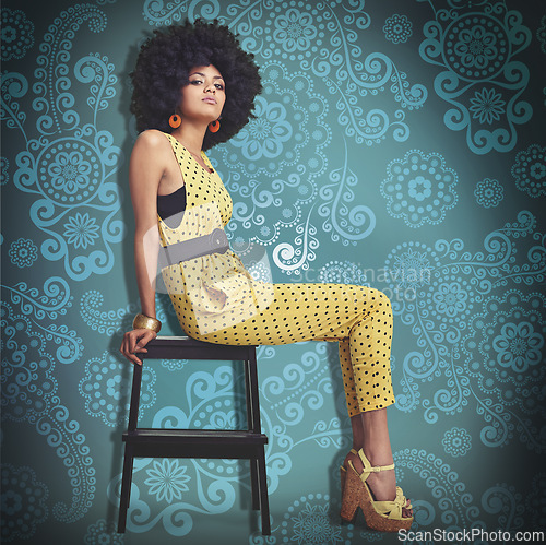 Image of Portrait, young woman and fashion in 70s retro colour jumpsuit and sitting on chair. African trend, elegant model pretty in vintage outfit, big curly hair and wedge heels on cool pattern background