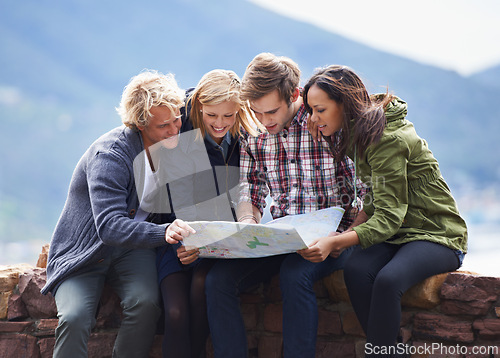 Image of Happy people, friends and map on stone wall for direction, location or planning next destination. Young group looking or checking route, path or spot for holiday weekend or outdoor vacation in nature