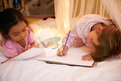 Image of Kids, color pencil and drawing on bed for sleepover, creative and relax in bedroom for weekend. Young girls, playing and learning art in book at night, friends and bonding by fairy light in pyjamas