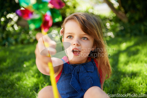 Image of Toy, girl and child playing with windmill on grass in nature, relax and having fun on lawn outdoor. Park, garden and young kid with pinwheel on summer vacation closeup for recreation, game or leisure