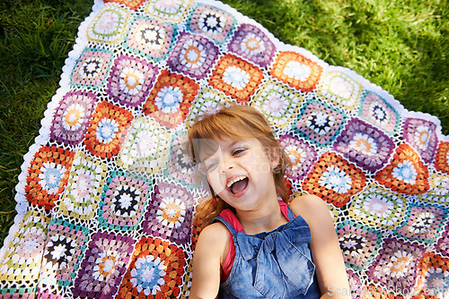 Image of Laughing, top view and kid on blanket outdoor on grass in nature, smile and relax in summer. Funny, above and face of girl child on lawn with excited facial expression for comedy, joke and humor