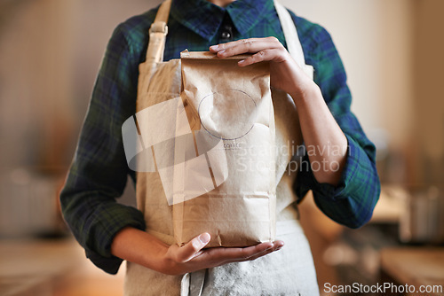 Image of Barista woman, hands and bag while in an apron in background at home. Close up of female worker wearing pinafore and holding craft paper order while packaging coffee beans as small business owner