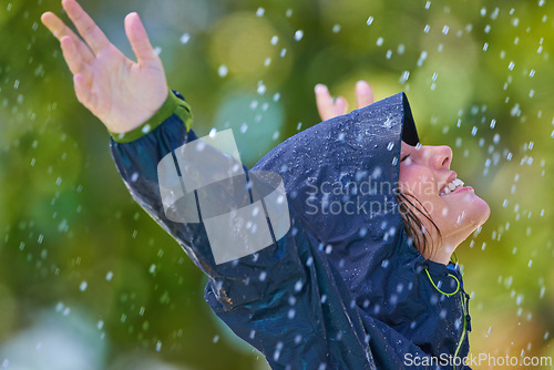 Image of Woman, rain and freedom with a smile from winter climate, water and weather outdoor in a park. Happy, travel and female person with jacket for cold on holiday and vacation with raincoat and joy