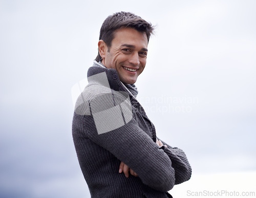 Image of Man, portrait and happy with arms crossed or sky for relax, travel and winter adventure on holiday or vacation. Person, tourist and face with smile in nature or outdoor for fresh air and wellness