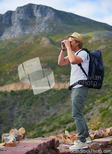 Image of Man, traveler and binoculars with backpack for sightseeing, outdoor travel or hiking on mountain in nature Young male person, hiker or tourist with bag or optical instrument for view, vision or scope