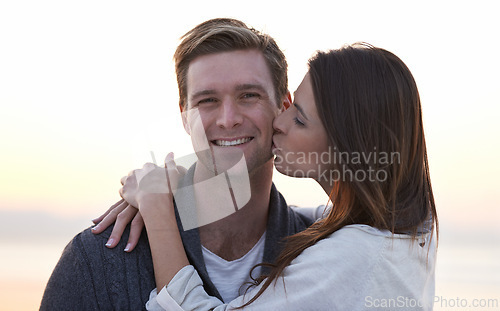 Image of Love, kiss and couple on beach at sunset for tropical holiday adventure, relax and bonding together. Commitment, happy man and woman on romantic date with ocean, evening sky and embrace on vacation.