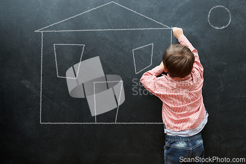 Image of Kid, drawing and art of house on chalkboard of preschool as young student in classroom. Little boy, creative and imagination for sketch of home on dark background of blackboard for real estate