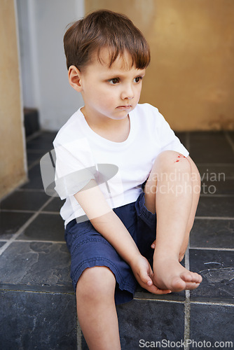 Image of Little boy, sitting and injury on knee in home and accident, ache and with blood from cut. Young child, sad and holding hurt leg up with hand on foot, pain and sore on bruise with fear of trouble