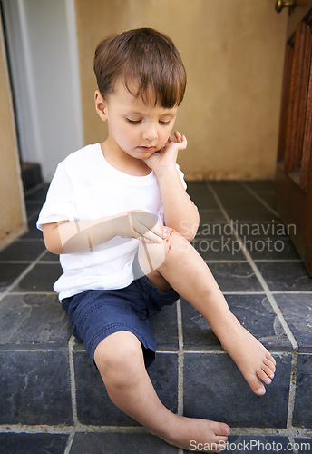 Image of Small child, injured and bleed on knee from fall, scratch and youth in pain from bruise on leg. Young boy, sitting and stairs outdoor house, looking and wound on skin from accident, touch and hand