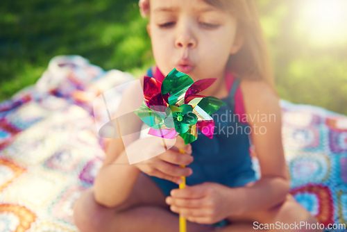 Image of Young girl, picnic and blowing pinwheel, garden and enjoying freedom of outside and happy. Colourful little child, backyard and summer for playing, toy and windmill for school holidays and happiness