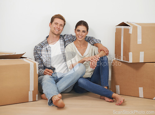 Image of New home, portrait and happy couple with boxes in living room, moving and relax for investment in real estate. Man, woman and proud homeowners with package in property and mortgage loan for apartment