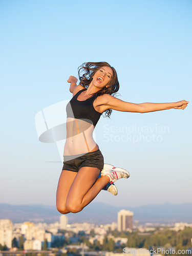 Image of Woman, exercise and jump to air of sky in city of buildings on the roof with mouth open in happiness. Person, workout and fitness for health with energy for freedom of sports, wellness and athletic