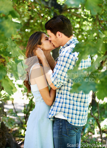 Image of Couple, love and kissing in nature with trees in forest for peace and summer vacation. Holiday, affection and young man and woman bonding with commitment for a natural relationship on honeymoon
