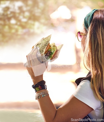 Image of Hand, fast food and woman eating burger closeup outdoor for hunger, takeaway or craving in summer. Hamburger, lunch or snack with hungry young person holding a fresh beef bun for cuisine or meal