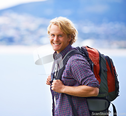 Image of Man, trekking and portrait on mountains for travel, adventure and wellness by ocean, sea and vacation in Europe. Face of an excited, young person with backpack for hiking, explore and outdoor journey