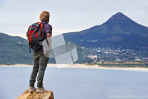 Image of Man, backpack and hiking on mountain by ocean for travel, sightseeing or outdoor journey in nature. Rear view of male person, hiker or tourist with bag on rock for trekking, fitness or adventure