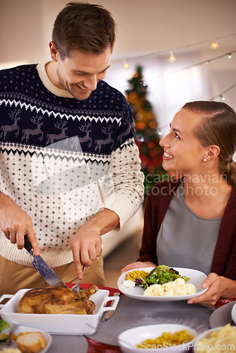 Image of Christmas, happy couple and eating dinner in home, smile or bonding together at party. Xmas, man or woman at table for food at festive celebration, relax or people on holiday cutting chicken for meal