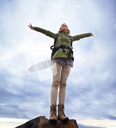 Image of Woman, hiking and freedom on mountain top for travel, success and achievement or fresh air on cloudy sky. Young person in backpack and stretching arms for trekking, journey or adventure in low angle