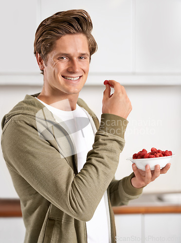 Image of Smile, portrait and man with raspberries in kitchen of home for diet, health and wellness. Happy, confident and male person eating fruit for fresh, organic or nutrition snack in modern apartment.