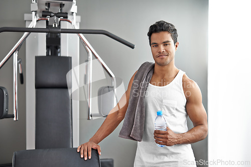 Image of Gym, machine and portrait of man with water bottle for recovery after exercise for body building. Healthy, fitness and person relax after workout with hydration for benefits to muscle and wellness