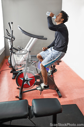 Image of Exercise bike, man and drinking water in a gym, fitness and endurance with nutrition and progress. Workout, bodybuilder and person with a bottle and wellness with cycling and cardio with a challenge