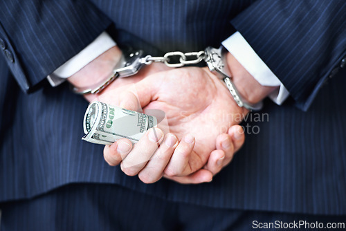 Image of Business person, hands and money with handcuffs for bribe, secret or corruption in financial crime. Closeup or rear view of employee with roll of cash, paper or laundering finance in bribery or fraud