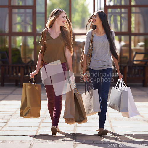 Image of Women, friends and walking with shopping bag or talking of fashion, sale and discount outdoor by store, mall or city. Young and happy people with style, clothes and luxury for commerce or retail