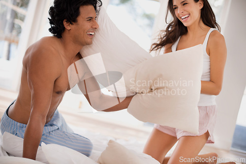 Image of Pillow, fight and couple on bed with happy battle in home together playing a game in morning. Silly, challenge and people with energy in bedroom and love in marriage with fun bonding in relationship