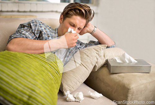 Image of Virus, influenza or man sneezing into tissue on sofa with cold, bug or hay fever at home. Flu, allergies or person with toilet paper for viral infection, bacteria or coughing with sinusitis in house