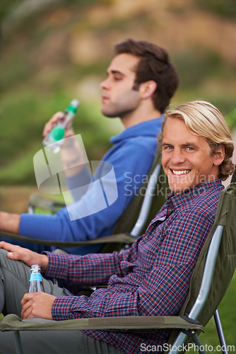 Image of Camping, man and portrait with drinks for relax on grass in nature with happiness for holiday and vacation. People, smile and alcohol at campsite in woods for adventure, travel and bonding in forest