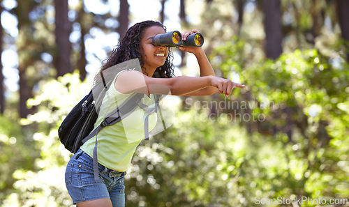 Image of Happy girl, binoculars and pointing in nature with backpack for sightseeing, explore or outdoor vision. Young female person, child or teenager enjoying adventure, bird watching or search in forest