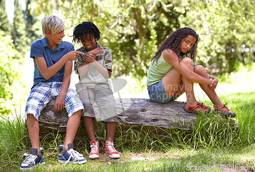 Image of Nature, bullying and boys with girl in outdoor field, woods or forest laughing and teasing. Rude, upset and cruel young children sitting on tree trunk in garden on vacation, holiday or weekend trip.