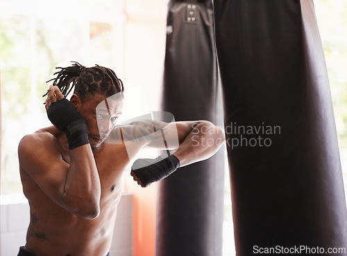 Image of Fitness, punching bag and black man in boxing gym for exercise, challenge or competition training. Power, muscle and serious champion boxer at workout with confidence, fight and energy in sports club