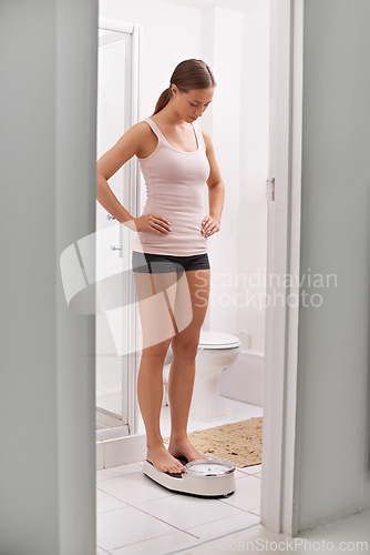 Image of Scale, weighing and woman in bathroom at her home for body fitness, diet or workout results. Health, wellness and young female person checking size on balance tool for weight loss in modern apartment